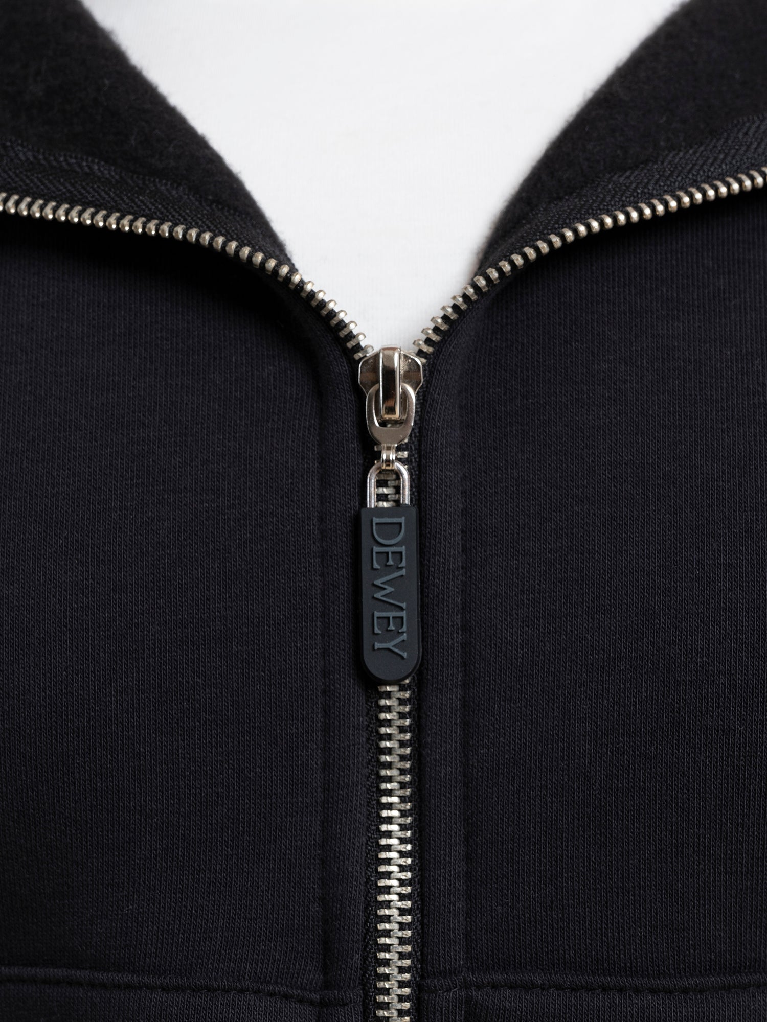 Close-up image of a black DEWEY TOBY full zip hoodie. The zipper is partially closed, with the zipper pull tab labeled 